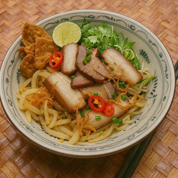 A bowl of Hội An's specialty noodle dish, Cao Lầu. The thick, chewy noodles are topped with slices of roasted pork belly, fresh herbs, and crispy fried crackers.