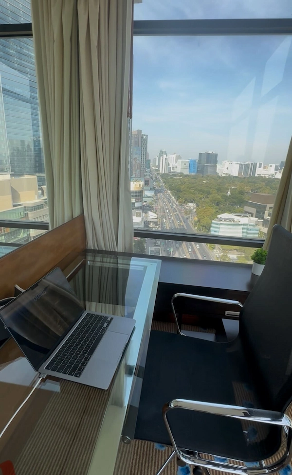 Digital nomad's desk setup with a laptop overlooking a bustling Southeast Asian city, illustrating the remote work lifestyle.