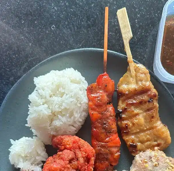 A plate of Thai street food essentials featuring sticky rice and grilled pork skewers (Moo Ping)