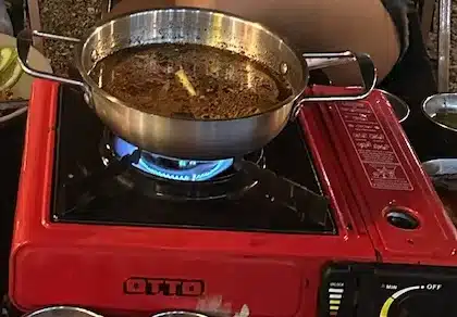 enjoying a Thai hot pot dinner cooked on a portable gas stove at an outdoor street food market at night.