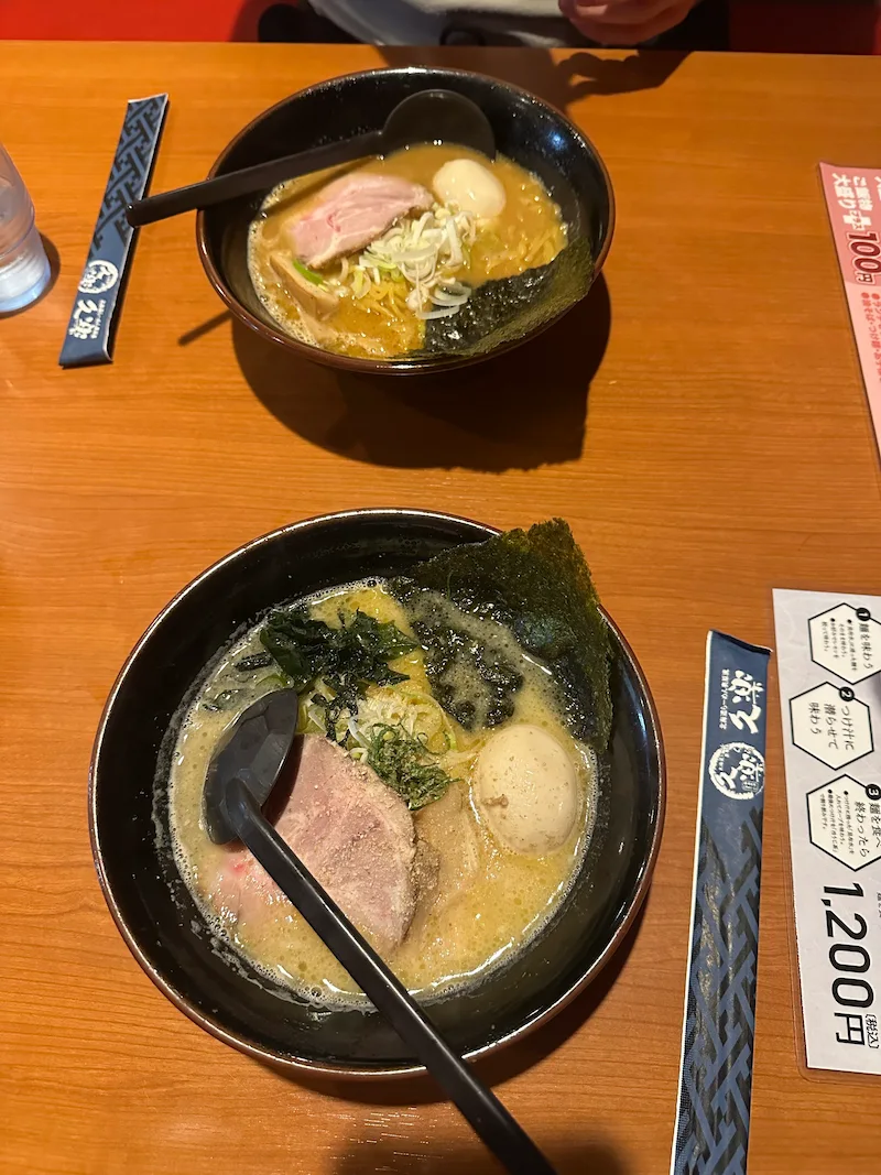 Two steaming bowls of authentic Hokkaido ramen on a wooden table at a roadside restaurant, featuring rich broth, chashu pork, and a soft-boiled egg.