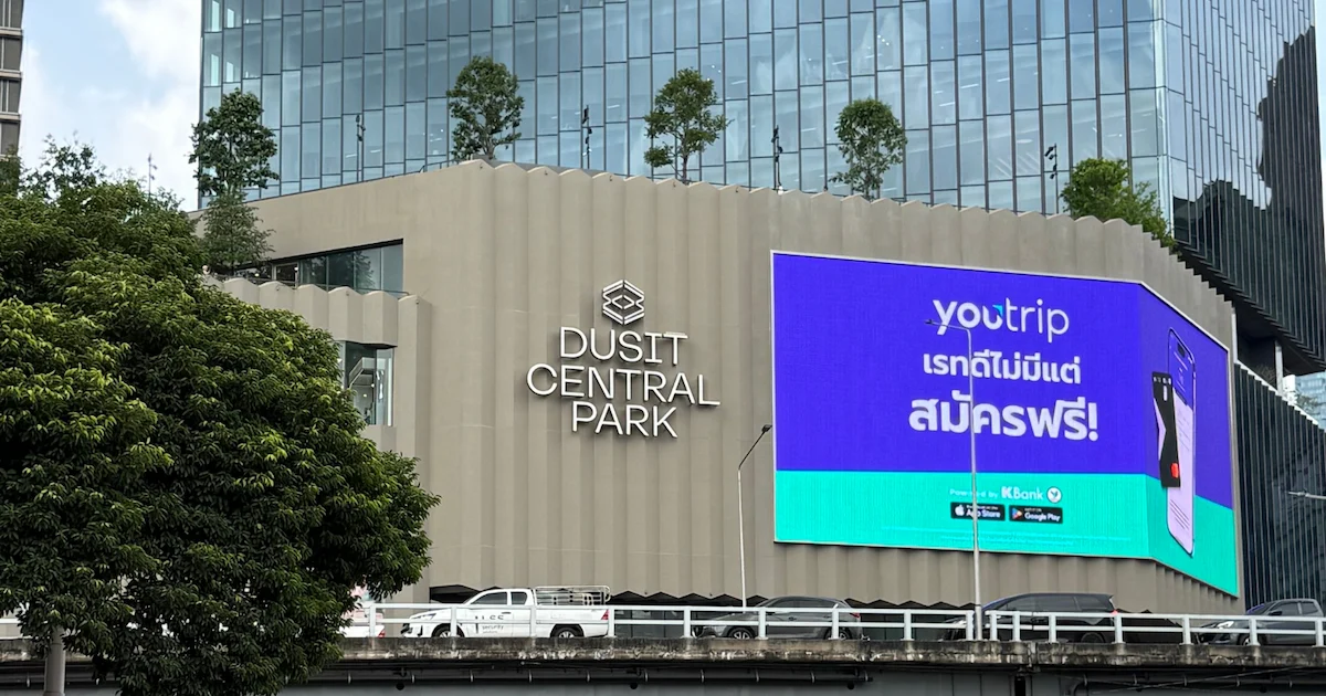 The modern, beige facade of the Dusit Central Park building in Bangkok. The mall's name is displayed in silver lettering next to a large, bright digital screen.