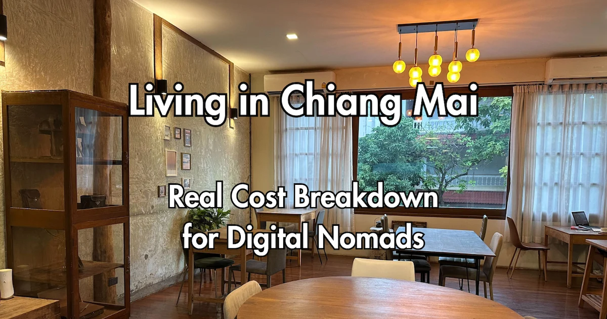 Interior of a cozy, warm-lit cafe in Chiang Mai featuring wooden tables, vintage decor, and a large window overlooking greenery, with text overlaying the image that reads "Living in Chiang Mai: Real Cost Breakdown for Digital Nomads."