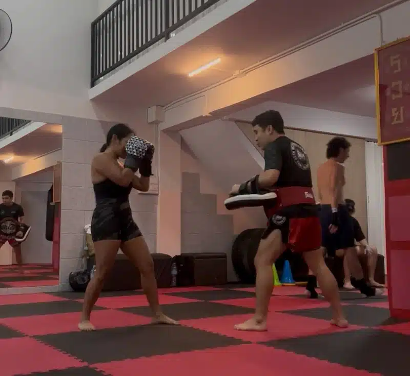 A woman training Muay Thai with a trainer at a local gym, a popular and affordable fitness activity for expats living in Thailand.