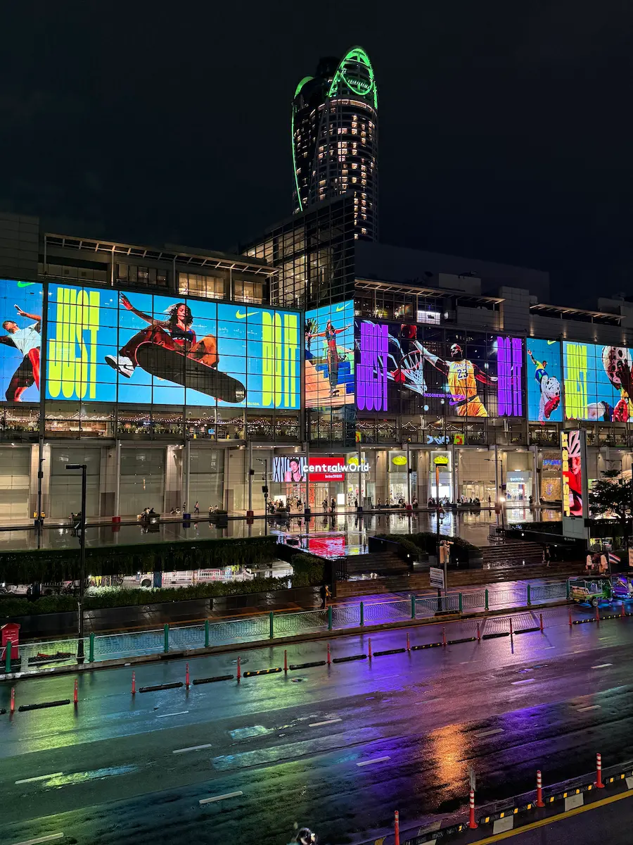 Another dynamic night shot of CentralWorld's exterior and its giant digital billboards. The iconic, glowing Centara Grand hotel tower rises in the background.