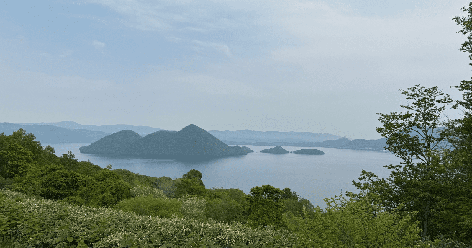 A panoramic view of Lake Toya, with a large, forested island dominating the center of the lake. Photo by Ann