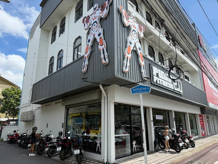 Picture of the building, parking and entrance area of Pump Fitness 2.0 in Chiang Mai, Thailand. The picture was taken in front of the building and shows the whole gym.