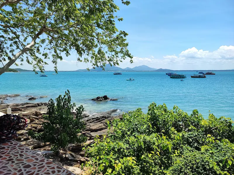 High-angle view of a turquoise bay on Koh Samet island with lush green hills and a few boats.
