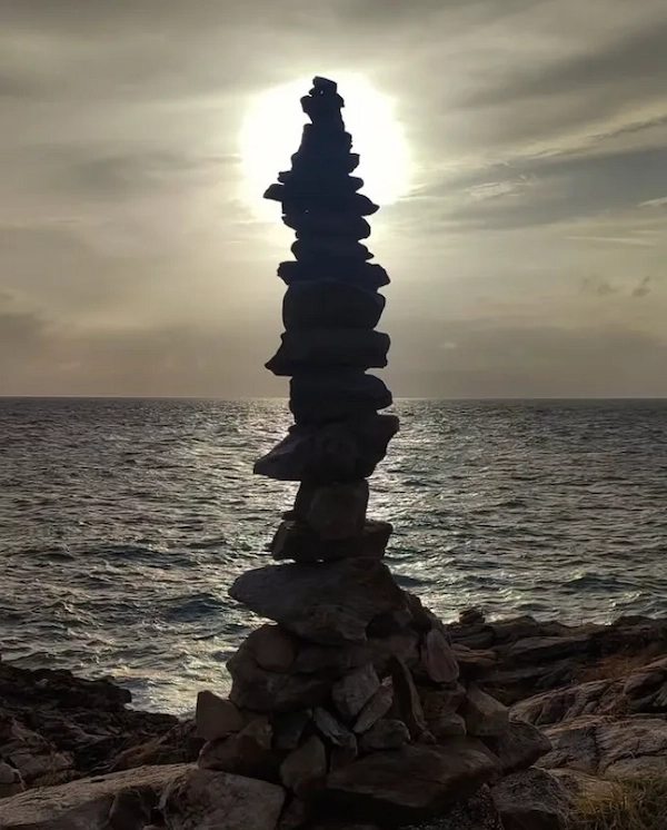 A stacked rock cairn on the beach at Laem Toei, Koh Samet, during a colorful sunset.