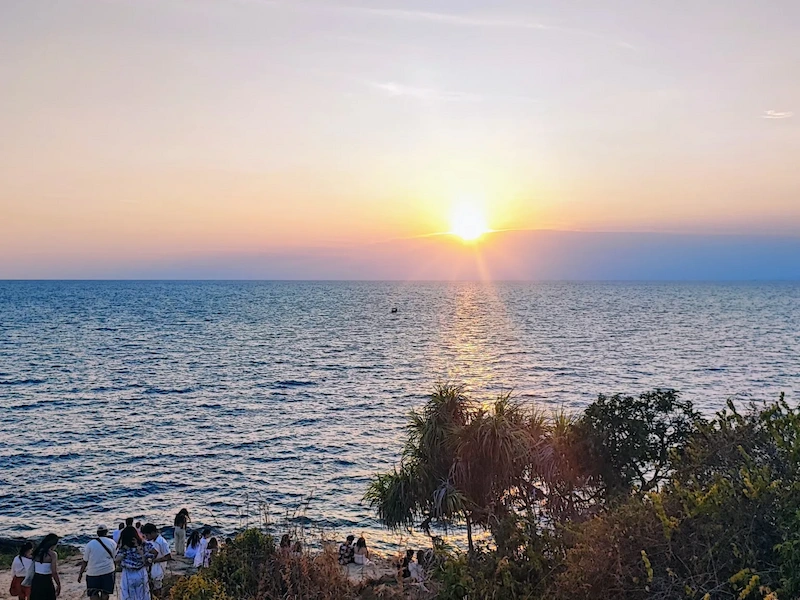A solo traveler watching a vibrant orange sunset over the ocean from the Koh Samet island viewpoint.