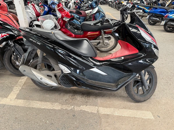 Picture of a black/red Honda PCX 160 in a parking lot in Thailand.