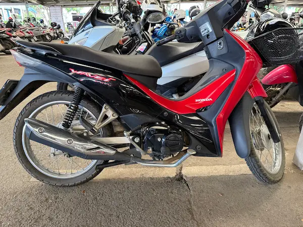 Picture of a red/black Honda Wave 110i in a parking lot in Thailand.