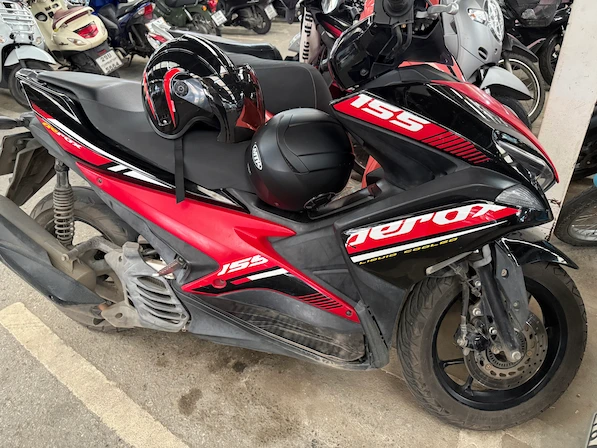 Picture of a red/black Yamaha Aerox 155 in a parking lot in Thailand.