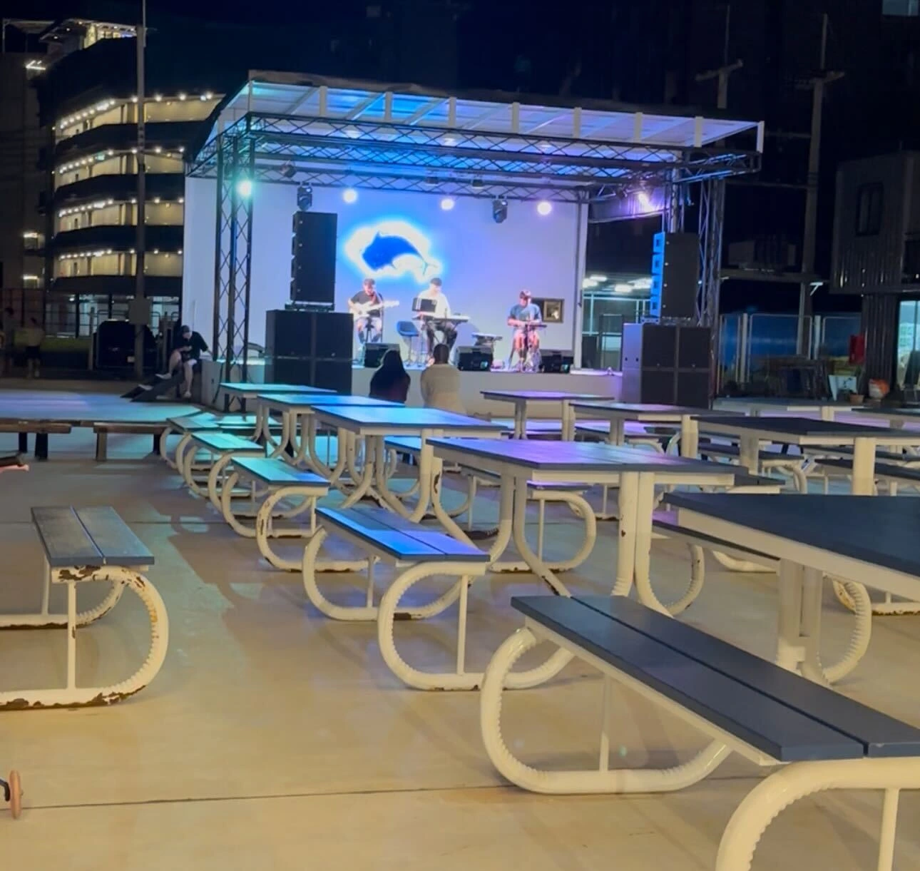A live band performs on a brightly lit stage in the entertainment area of the Blue Mountain night market in Krabi.
