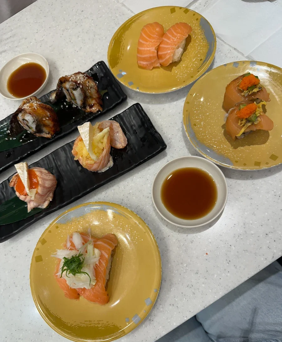 A delicious spread of various sushi plates on a white table. The assortment includes salmon nigiri on yellow plates and unagi rolls on black plates.