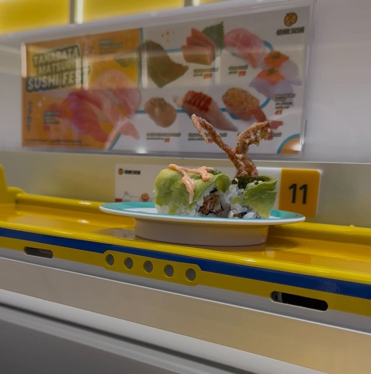A creative soft-shell crab and avocado sushi roll arriving at a table on the yellow track delivery system at Genki Sushi.
