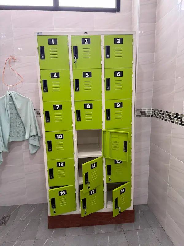 A set of bright lime-green lockers in the changing room of Get Well Fitness gym. Some of the locker doors are open, while others are closed. A light blue towel is hanging on a hanger next to the lockers.