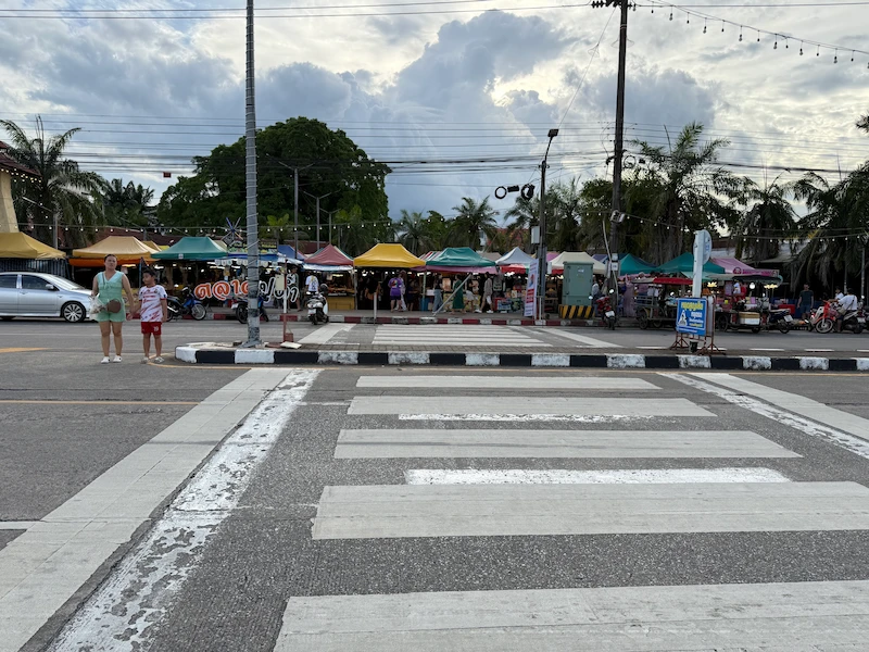 The exterior view of the Krabi Town market from across the street, showing the roadside setup with colorful tents and local traffic.