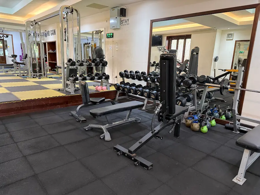 The free weights area at PUSH Fitness. The space is equipped with multiple dumbbell racks, weight benches, and a barbell press station. A large mirror on the wall reflects the equipment and enhances the sense of space. A collection of colorful kettlebells is on the floor to the right.