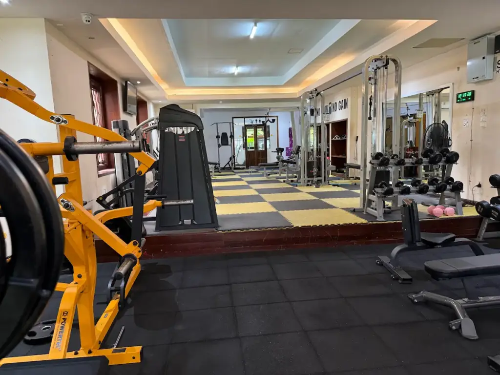 An interior view of PUSH Fitness, showing a variety of strength training equipment. In the foreground is an orange plate-loaded machine on a black rubber floor. The background area is slightly elevated and has a checkerboard pattern of black and yellow floor mats, with more gym machines.