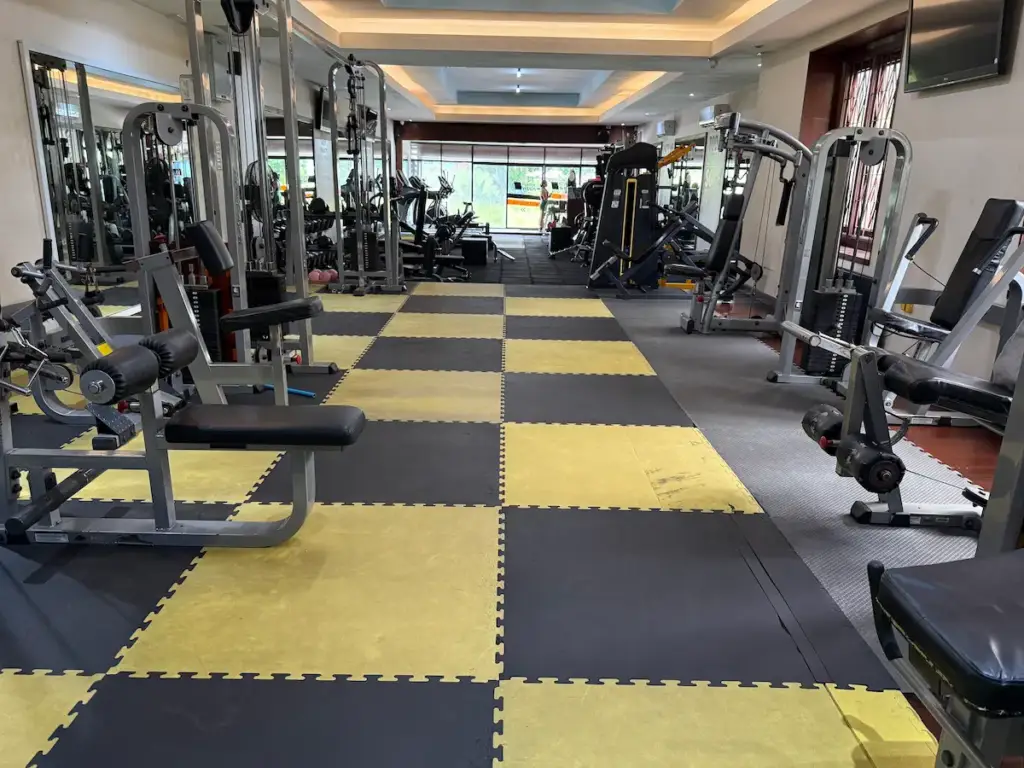A wide view of the interior of PUSH Fitness, highlighting the layout with a central walkway of yellow and black checkered flooring. The gym is filled with a comprehensive range of selectorized weight machines for various muscle groups. Large mirrors line the walls, and windows at the far end let in natural light.