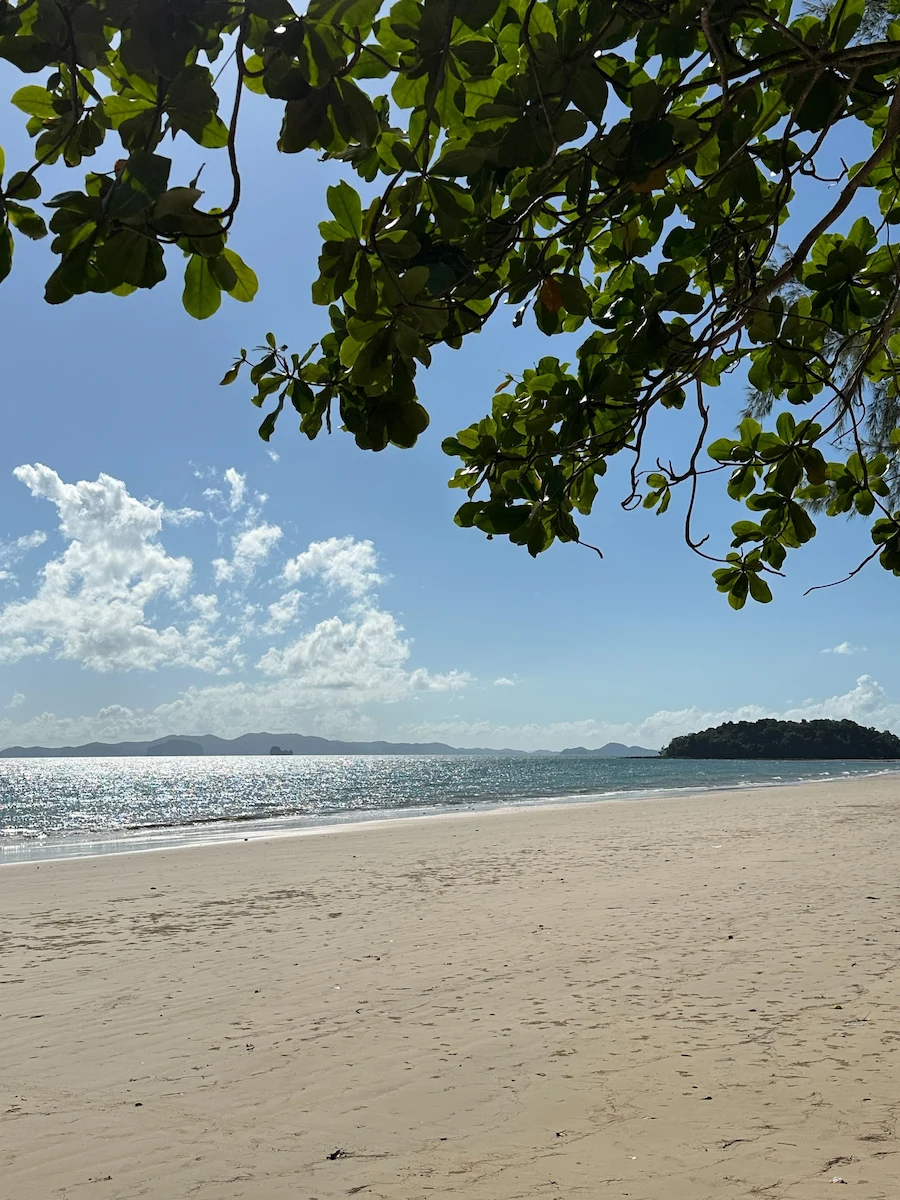 A peaceful, sunny day at Klong Muang Beach in Krabi, showing a wide expanse of clean sand and sparkling turquoise water under a blue sky.