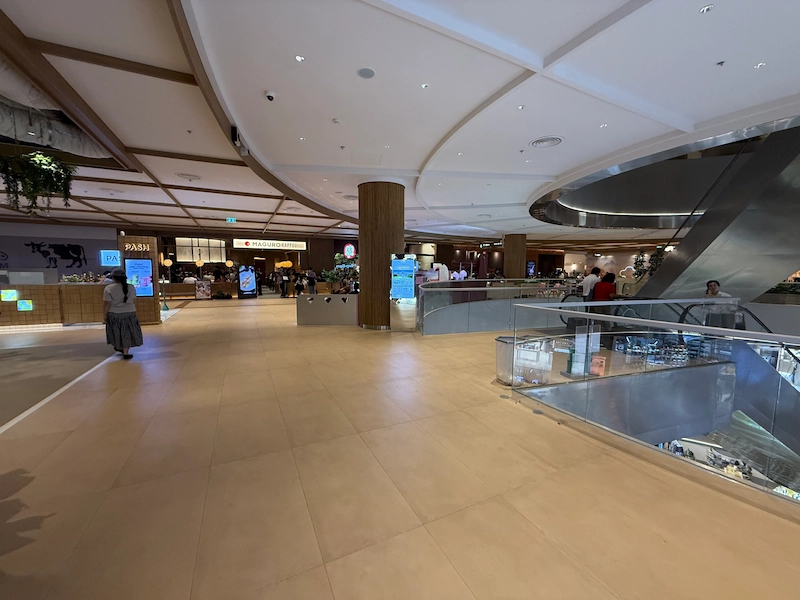 A wide shot of one of the spacious dining floors inside Dusit Central Park. The curved architecture and entrances to restaurants like Maguro are visible.