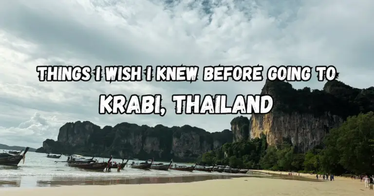 The title "Things I Wish I Knew Before Going to Krabi, Thailand" overlaid on a scenic photo of long-tail boats on a beach in front of Krabi's famous limestone cliffs.