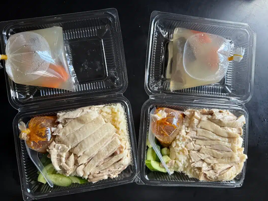 Two generous portions of chicken rice packed for takeaway, showcasing the large serving size and complimentary clear broth included with every order.