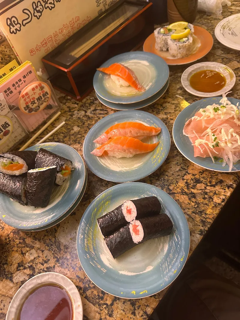 A spread of fresh sushi plates, including salmon nigiri and rolls, at a local conveyor belt sushi restaurant in Hokkaido.