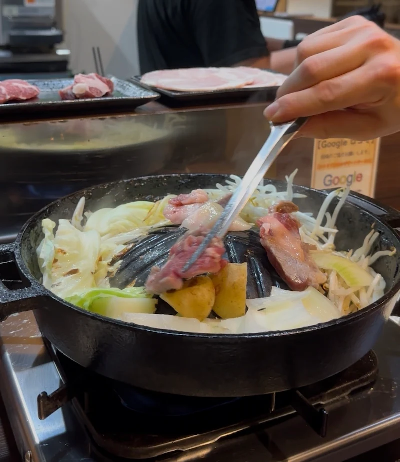 Grilling fresh lamb and vegetables on a traditional domed skillet for a delicious Genghis Khan BBQ dinner in Sapporo.