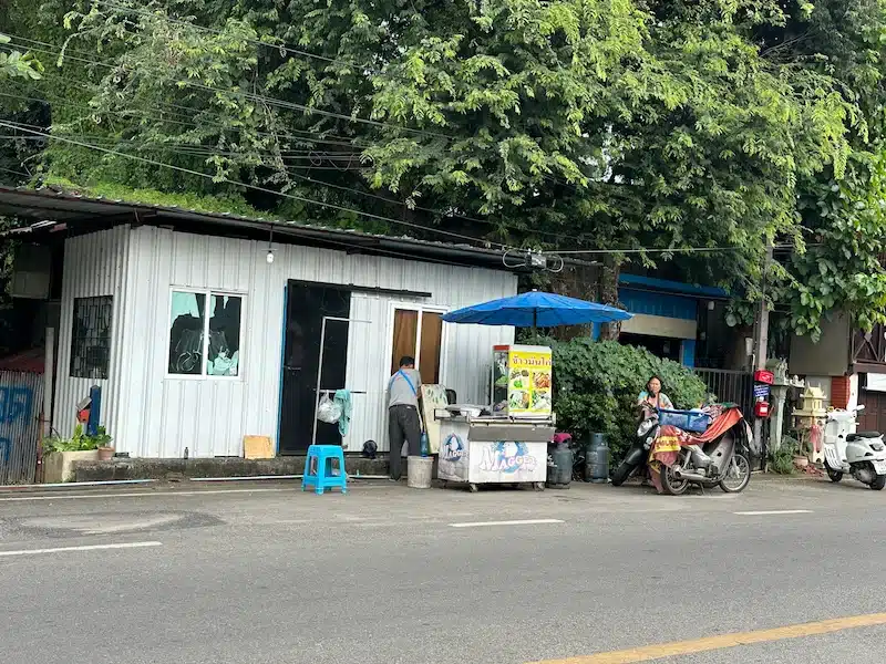 A view from across the road showing the humble white shack and the signature blue umbrella where the chicken rice couple sets up every morning.