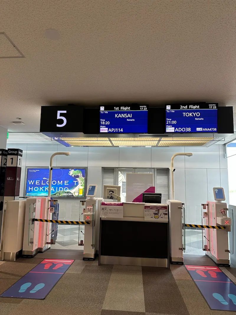 The departure gates at the airport showing flight status screens for Peach Aviation and Air Do flights heading to Kansai and Tokyo.