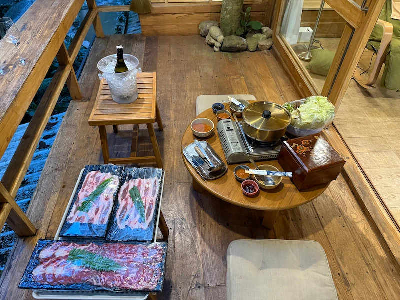 A private Shabu Shabu (hot pot) dinner setup on the wooden balcony at Woo Ma Ca Moo, featuring fresh meat, vegetables, and a bottle of wine on ice.