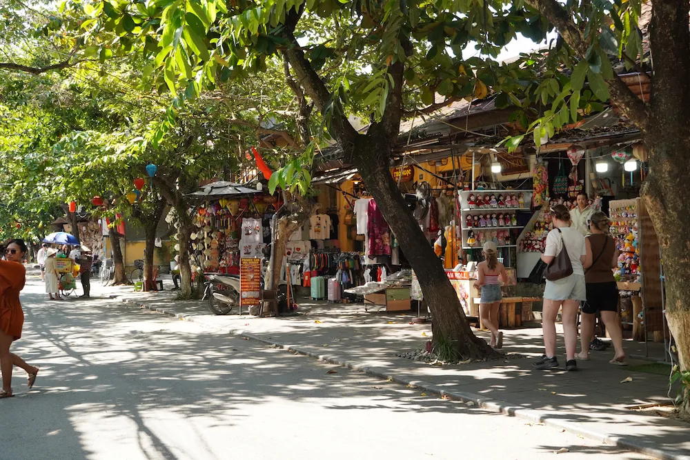 Shady tree-lined street with souvenir shops and market stalls in Hoi An Ancient Town, Vietnam