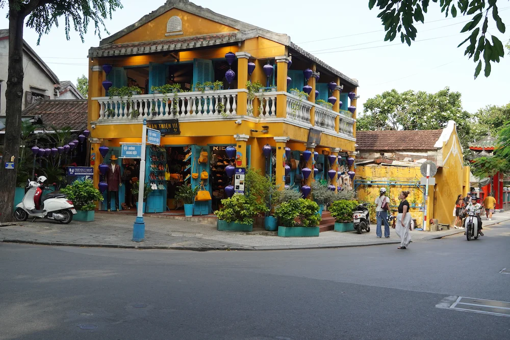 Yellow colonial house with potted palms beside the tiled roof of the Japanese Covered Bridge in Hoi An