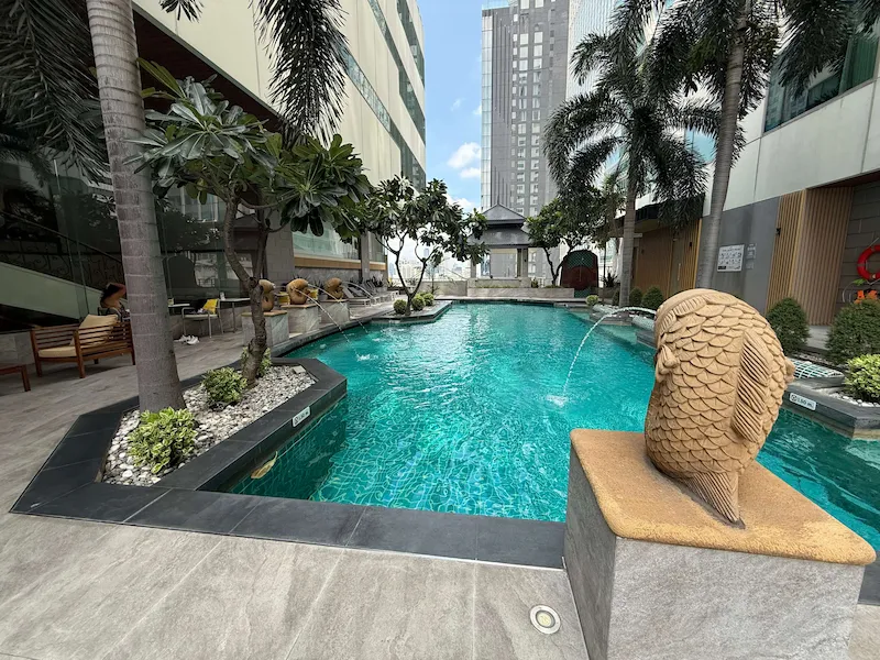 Outdoor swimming pool with palm trees and fish fountains at Jasmine City Hotel in Asok, Bangkok