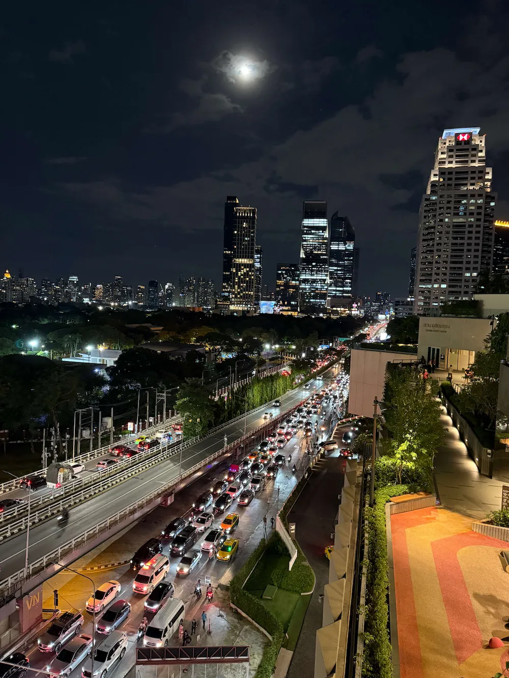 Night view over Lumpini Park and the Bangkok skyline from a rooftop garden