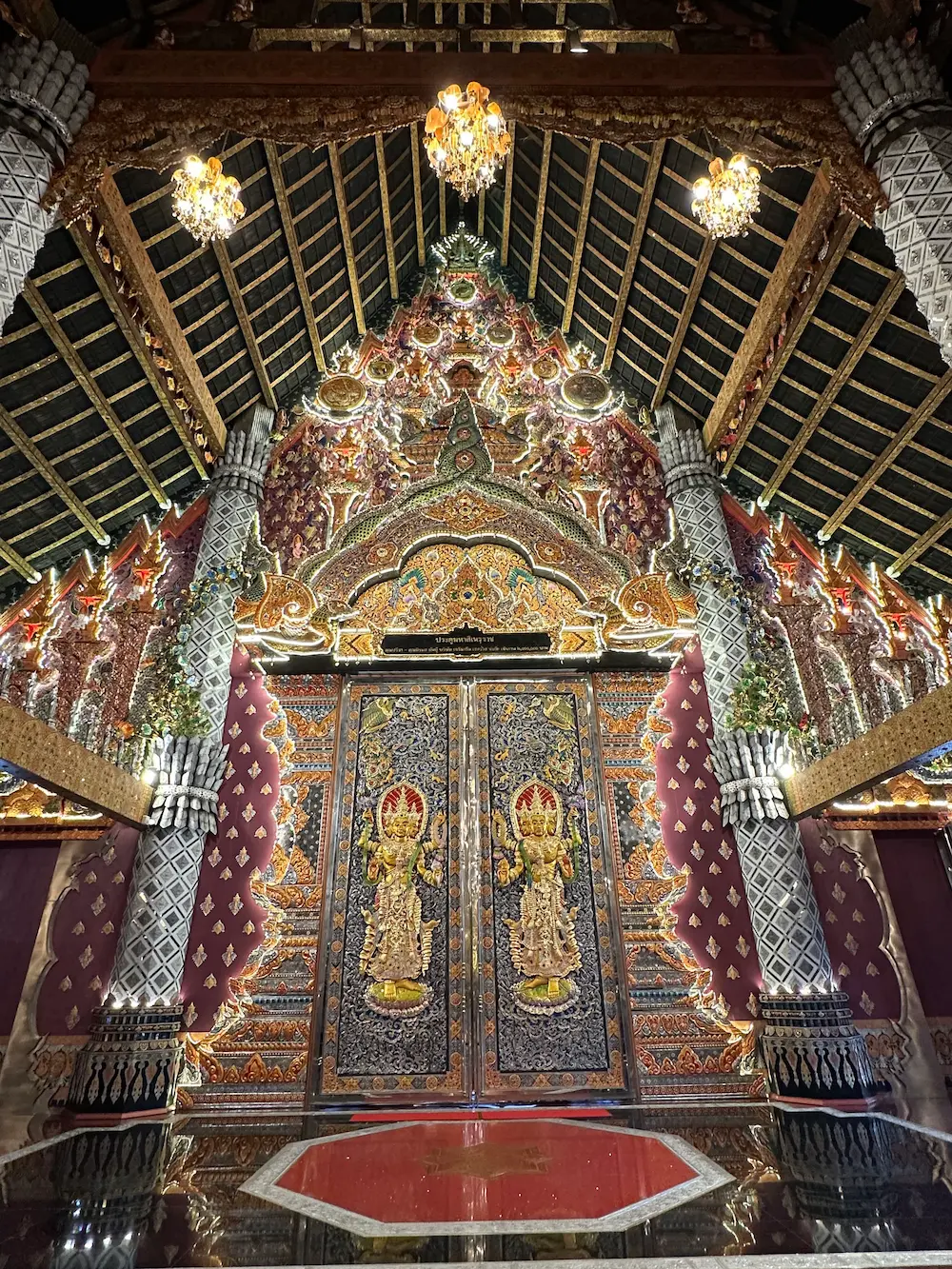 Grand door inside Wat Sri Don Moon's main hall, decorated with golden deities, mirror-tiled pillars, and chandeliers