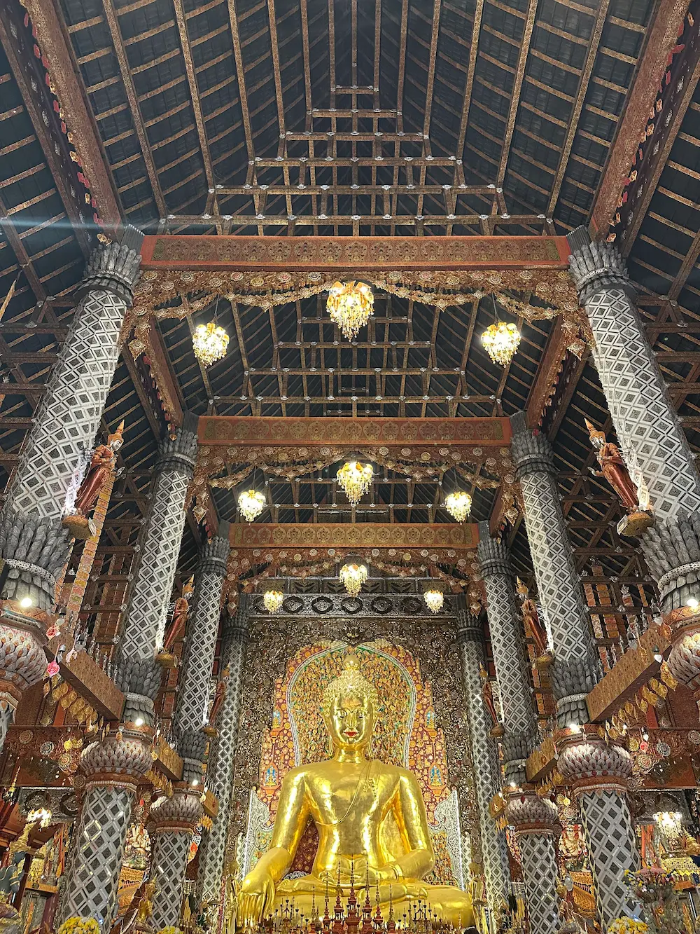Golden seated Buddha inside the main hall of Wat Sri Don Moon, Chiang Mai, beneath a wooden ceiling with chandeliers and mirror-tiled pillars