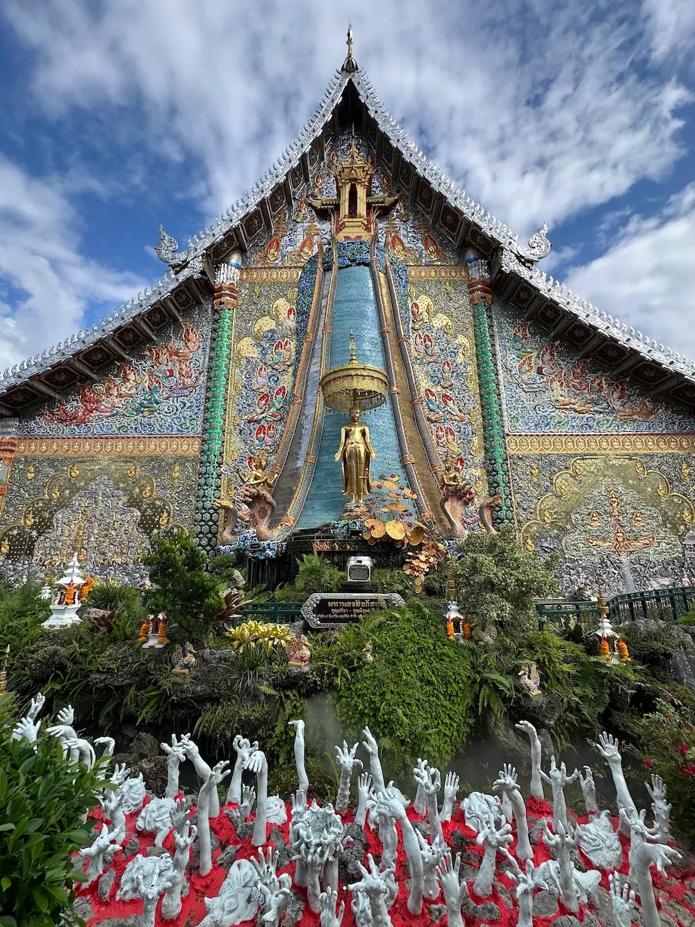Back wall of Wat Sri Don Moon's main hall, with a golden standing Buddha on a staircase from heaven and white "hands from hell" sculptures below